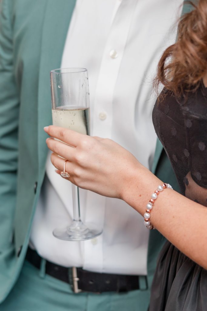 girl holding champagne with engagement ring on hand
