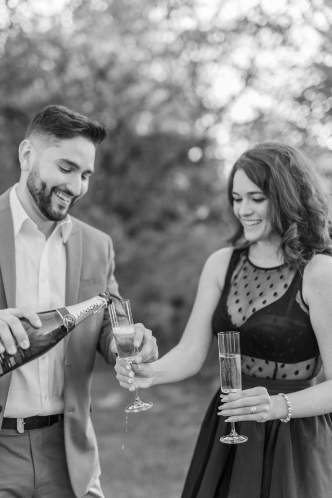 Black and white photo of newly enaged couple pouring champagne