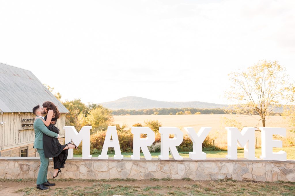 Guy and girl kissing in front of marry me sign