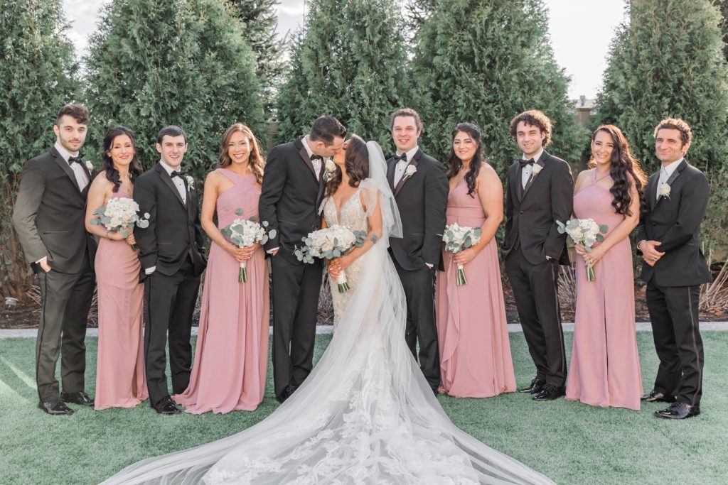 Wedding party win pink dresses and black tuxedos with kissing couple