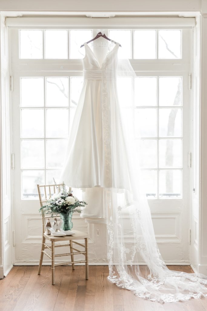 bridal gown hanging in window with lace veil