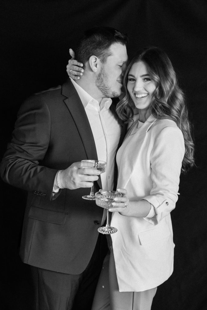 Black and white portrait of couple holding champagne glasses with black back drop