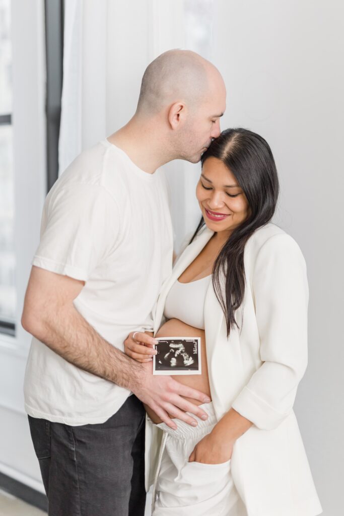 Women holding baby ultrasound while man kissing her