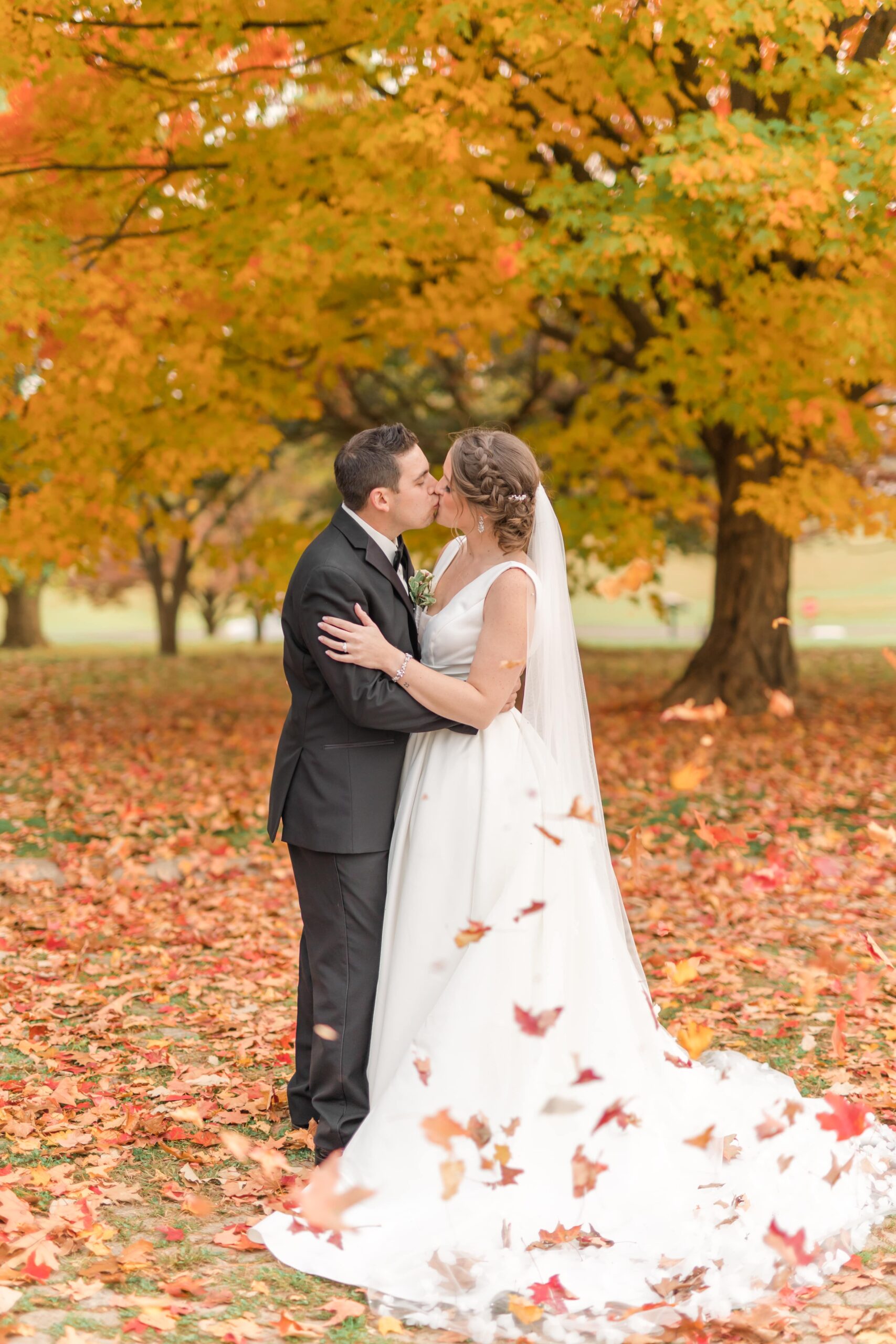 Bride and groom kissing in autumn leaves