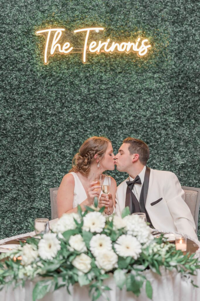 Bride and groom kissing at head table under neon sign